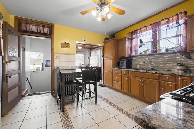 kitchen with dark stone countertops, light tile patterned floors, decorative backsplash, a sink, and ceiling fan