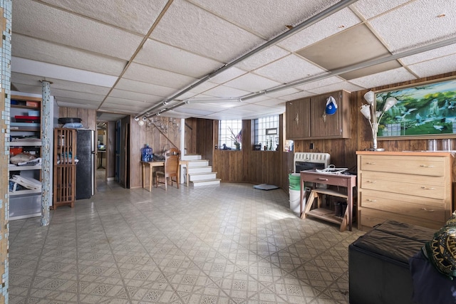basement with tile patterned floors, stairs, wooden walls, and a drop ceiling