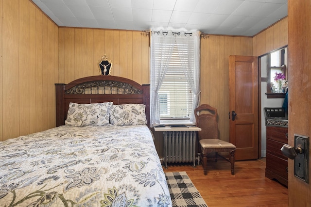 bedroom featuring radiator heating unit, wood finished floors, wooden walls, and multiple windows