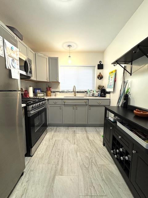 kitchen with gray cabinetry, stainless steel appliances, light countertops, and a sink