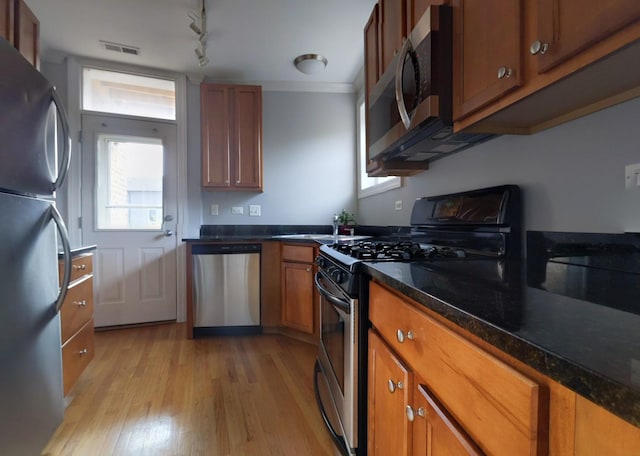 kitchen with light wood-style flooring, dark countertops, appliances with stainless steel finishes, and brown cabinetry