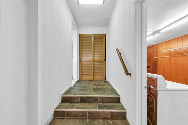 stairway featuring wooden walls, washer / dryer, and stone tile flooring