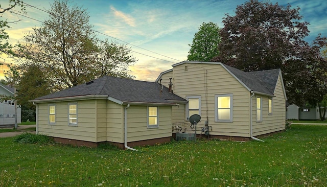 rear view of property featuring a yard, central AC unit, and a shingled roof