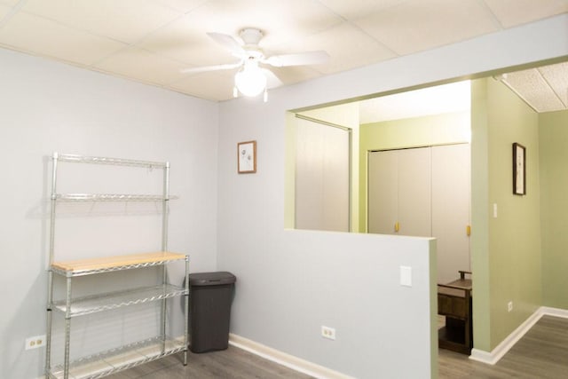 interior space featuring wood finished floors, ceiling fan, a drop ceiling, and baseboards