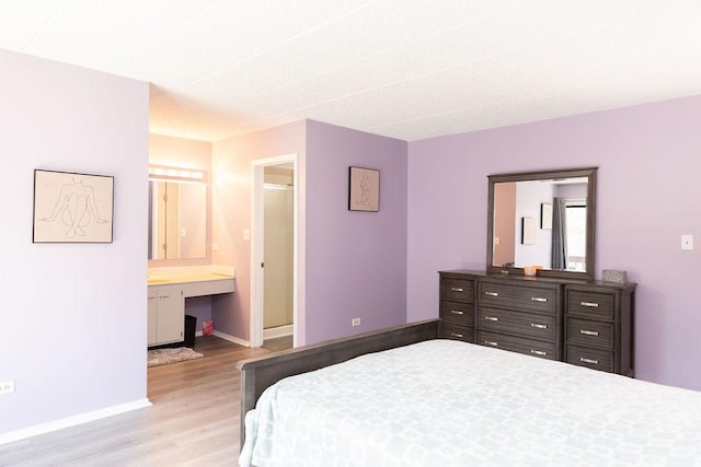 bedroom with baseboards, built in study area, connected bathroom, and light wood finished floors