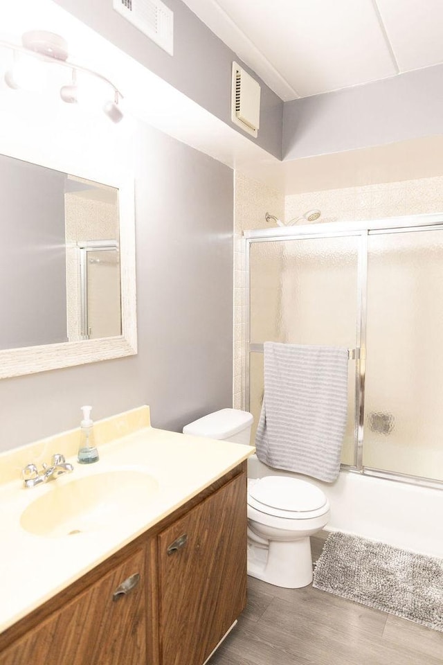 bathroom featuring wood finished floors, combined bath / shower with glass door, toilet, vanity, and visible vents