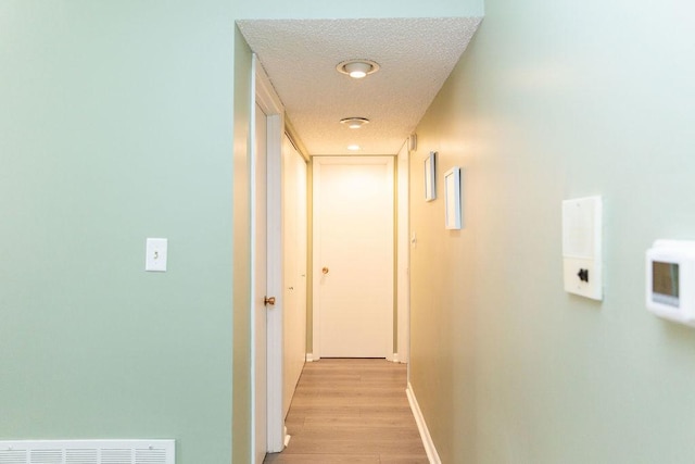 corridor with baseboards, visible vents, a textured ceiling, and light wood finished floors