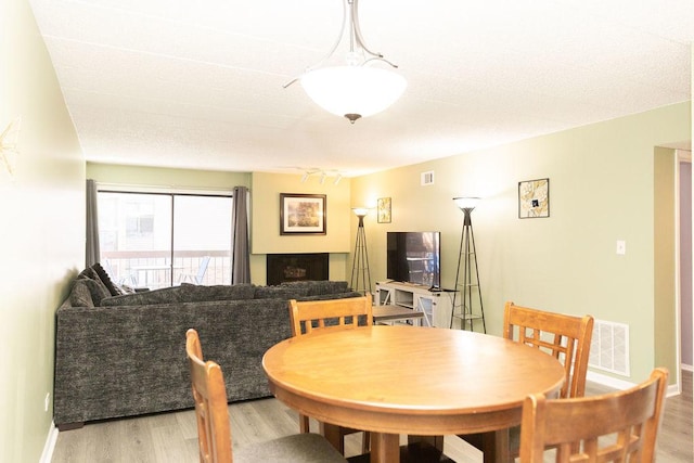 dining area with a fireplace, visible vents, baseboards, and light wood-style floors