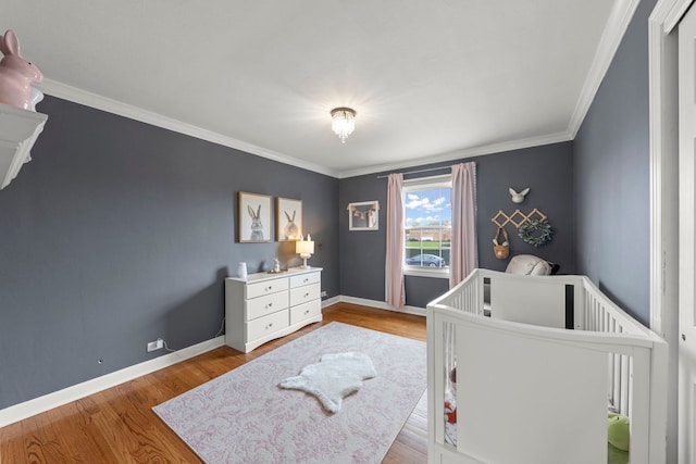 bedroom featuring crown molding, a nursery area, baseboards, and wood finished floors