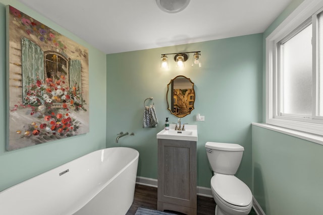 bathroom featuring vanity, a freestanding tub, wood finished floors, toilet, and baseboards