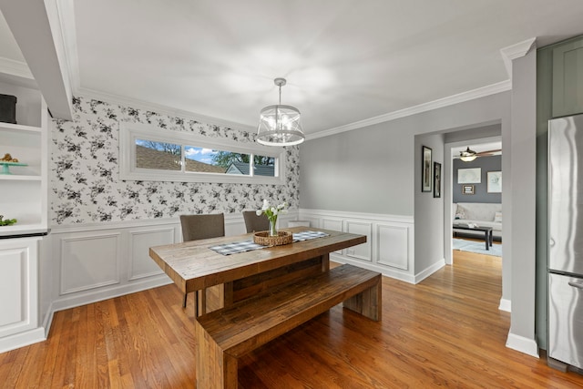 dining room featuring an inviting chandelier, a decorative wall, light wood-style floors, a wainscoted wall, and ornamental molding