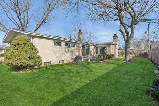 rear view of property with a chimney, fence, and a lawn