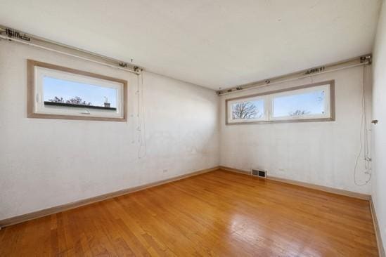 unfurnished room with baseboards, visible vents, and wood finished floors