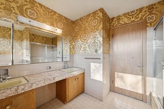 bathroom with double vanity, wainscoting, wallpapered walls, and a sink