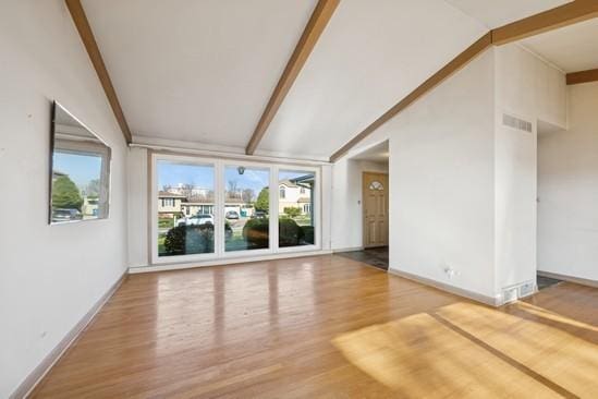 unfurnished living room with wood finished floors, plenty of natural light, visible vents, and vaulted ceiling with beams