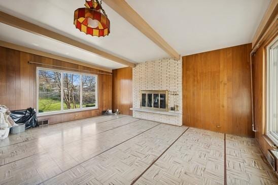 unfurnished living room with beamed ceiling, wooden walls, and a brick fireplace