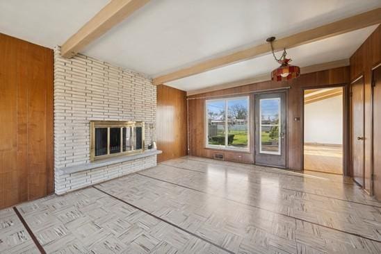 unfurnished living room featuring beam ceiling, wood walls, and a brick fireplace