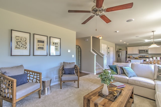 living area featuring ceiling fan, stairs, visible vents, light carpet, and baseboards