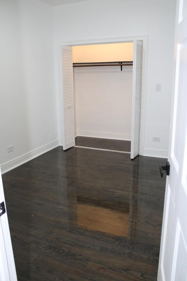 unfurnished bedroom with baseboards, dark wood-style flooring, and a closet