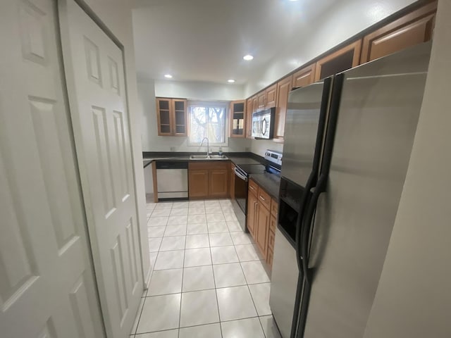 kitchen featuring light tile patterned floors, glass insert cabinets, a sink, dark countertops, and stainless steel appliances