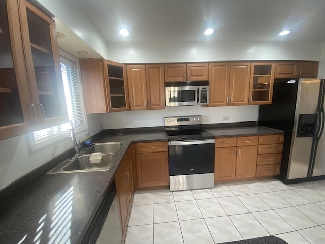 kitchen with appliances with stainless steel finishes, brown cabinets, glass insert cabinets, and a sink