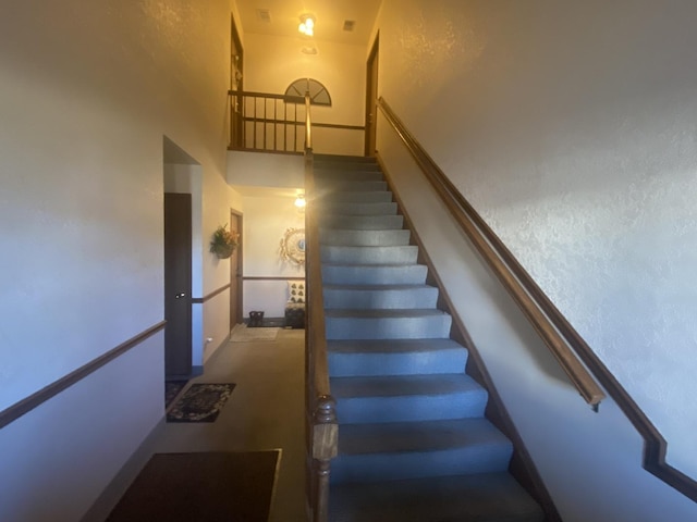 staircase with a towering ceiling and a textured wall