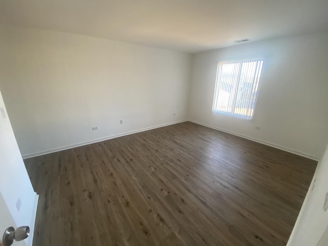 unfurnished room with visible vents, dark wood-style floors, and baseboards