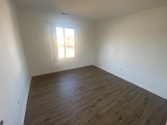 empty room featuring visible vents, baseboards, and dark wood-type flooring