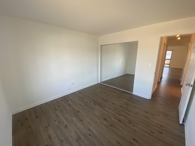 unfurnished bedroom featuring dark wood-style floors, baseboards, and a closet