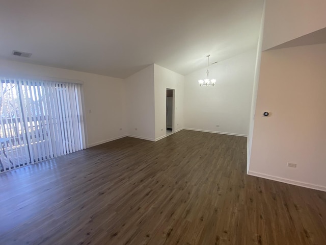 spare room with an inviting chandelier, dark wood-type flooring, visible vents, vaulted ceiling, and baseboards