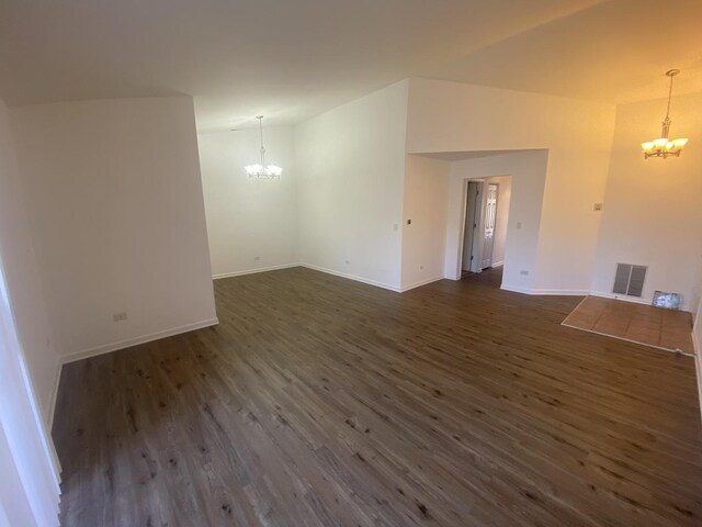 unfurnished living room featuring dark wood-style flooring, a chandelier, visible vents, and baseboards