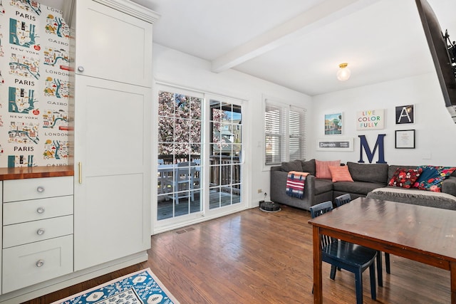 living area featuring visible vents, beam ceiling, and wood finished floors