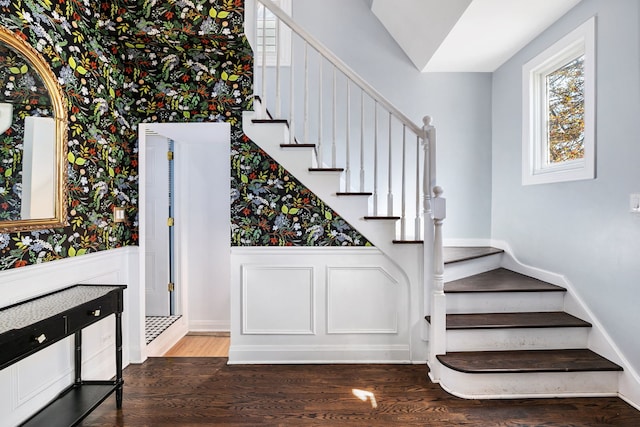 staircase with wood finished floors, a wainscoted wall, a healthy amount of sunlight, and wallpapered walls
