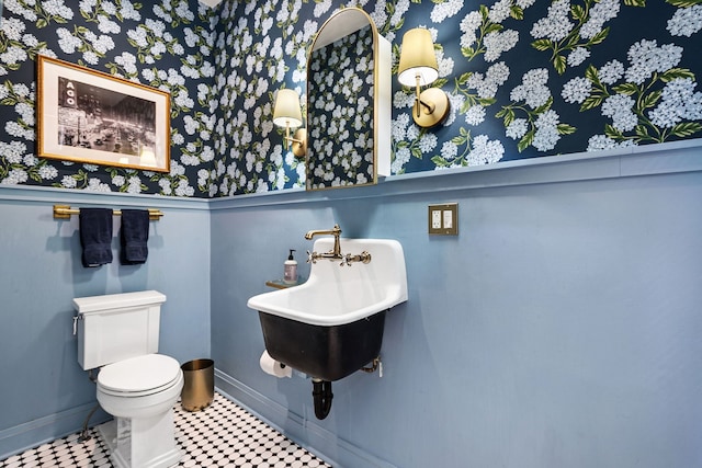 bathroom with baseboards, toilet, wallpapered walls, and a sink