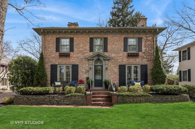 view of front facade featuring a chimney, brick siding, and a front yard