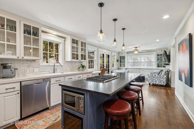 kitchen featuring stainless steel appliances, crown molding, a kitchen breakfast bar, dark wood-style flooring, and white cabinetry