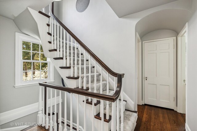 stairs with wood finished floors, lofted ceiling, and baseboards