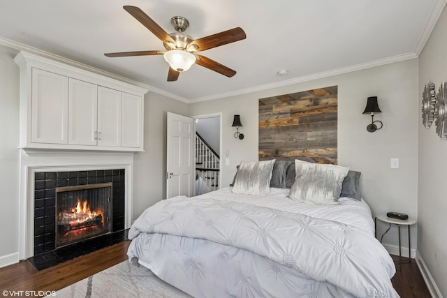bedroom featuring wood finished floors, a fireplace, ornamental molding, baseboards, and a ceiling fan