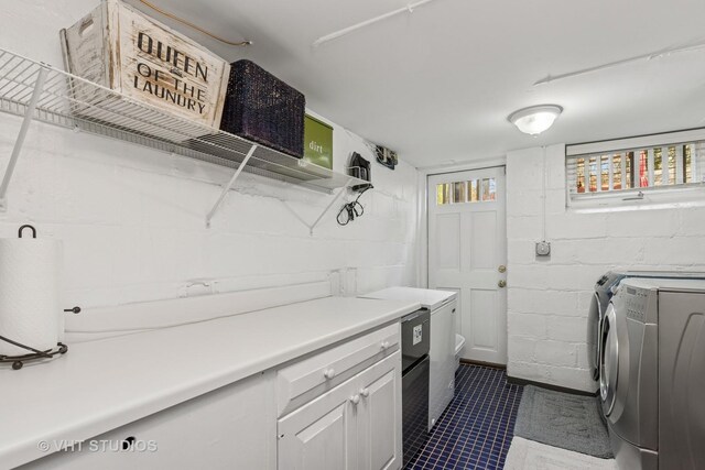 laundry room with washing machine and clothes dryer, concrete block wall, dark tile patterned flooring, and cabinet space