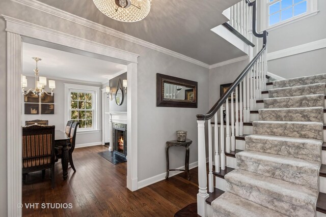 staircase with a chandelier, wood finished floors, baseboards, crown molding, and a high end fireplace
