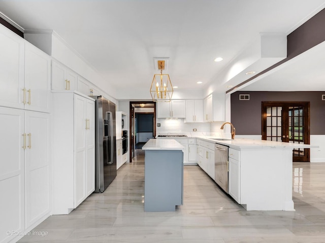 kitchen with appliances with stainless steel finishes, light countertops, a peninsula, white cabinetry, and a kitchen island