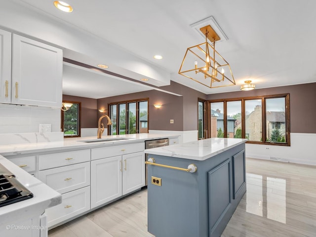 kitchen with a sink, light stone counters, a kitchen island, and white cabinetry