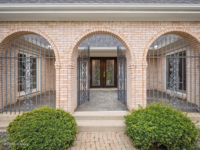doorway to property with brick siding, french doors, and a shingled roof