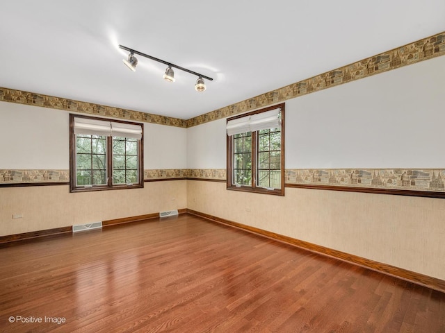 spare room with visible vents, wainscoting, wood finished floors, and a healthy amount of sunlight