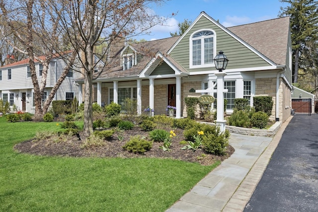 view of front of home featuring covered porch, a shingled roof, a front lawn, and stone siding