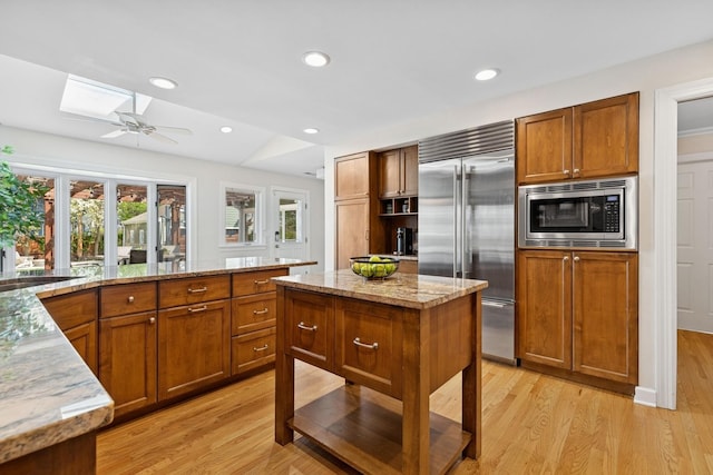 kitchen featuring brown cabinetry, light wood finished floors, built in appliances, and a skylight