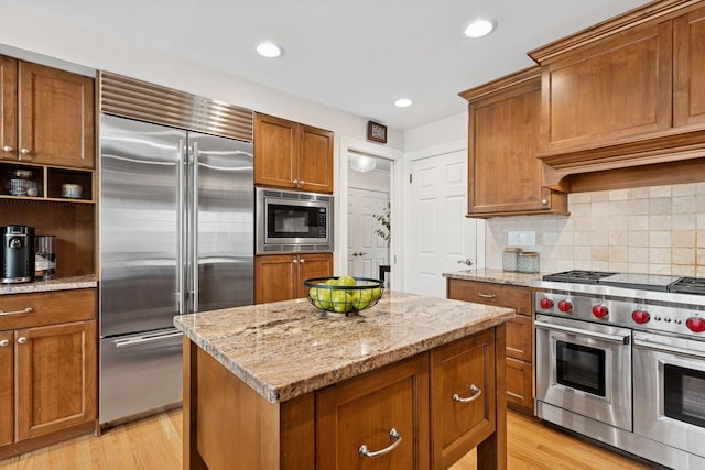 kitchen with built in appliances, brown cabinets, and light stone countertops