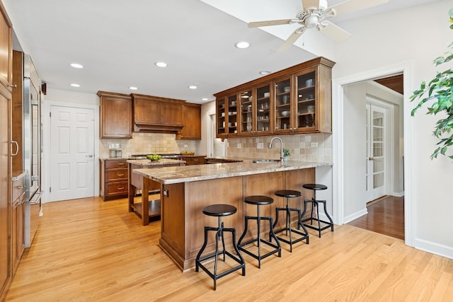 kitchen featuring a sink, decorative backsplash, a peninsula, and light wood-style flooring