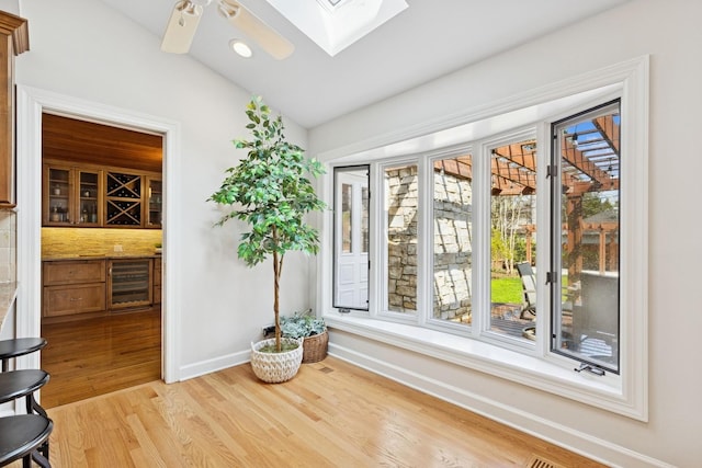 interior space with beverage cooler, baseboards, recessed lighting, vaulted ceiling with skylight, and light wood-style flooring