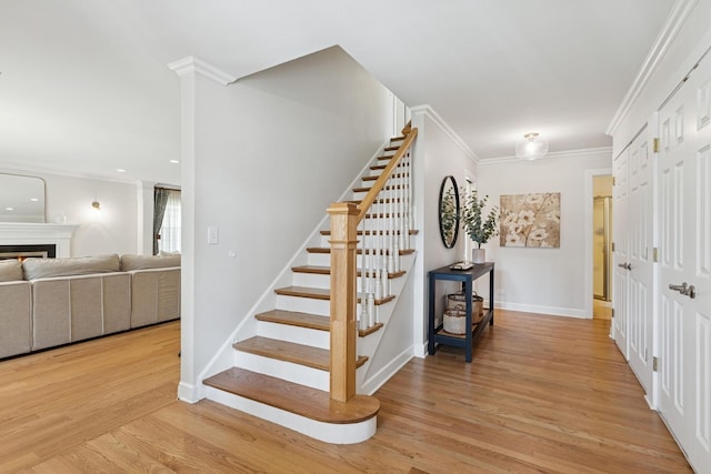 stairs with baseboards, ornamental molding, wood finished floors, and a warm lit fireplace